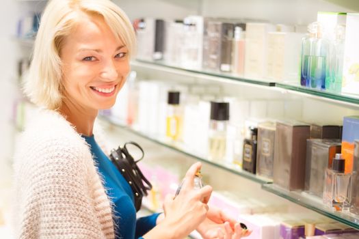 Cheerful elegant blond young woman testing cosmetics in perfumery.