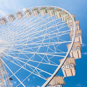 Ferris wheel of fair and amusement park.  White clouds in the blue sky in background.