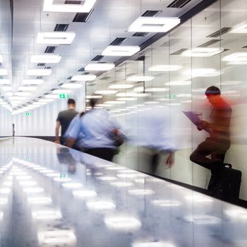 Business travelers  walking along contemporary illuminated airport terminal hall.