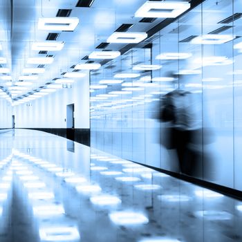 Blurred silhouette of a business traveler  walking along contemporary illuminated airport terminal hall.