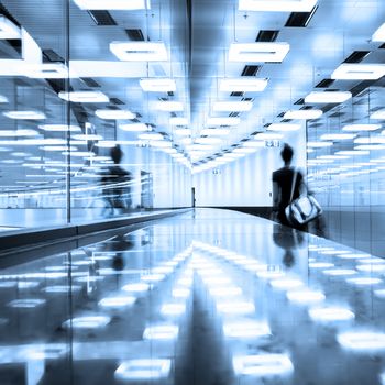 Blurred silhouette of a traveler walking down the contemporary illuminated airport terminal corridor.