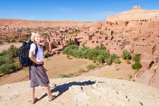 Adventurous woman in front of at Ait Benhaddou, fortified city, kasbah or ksar, along the former caravan route between Sahara and Marrakesh in present day Morocco.