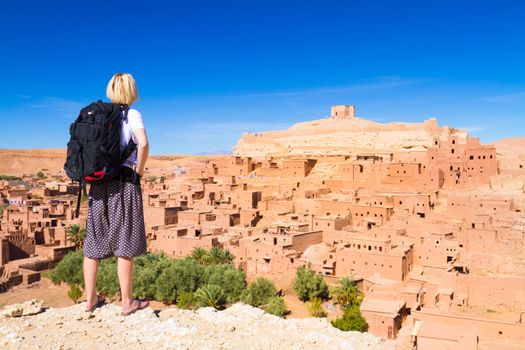 Adventurous woman looking at Ait Benhaddou, fortified city, kasbah or ksar, along the former caravan route between Sahara and Marrakesh in present day Morocco.