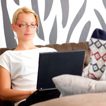 Relaxed, beautiful young woman sitting on sofa, using netbook