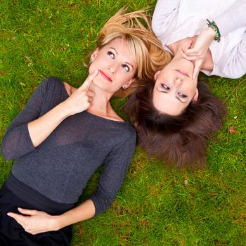 Two thoughtful girls lying in the grass have an smart idea.