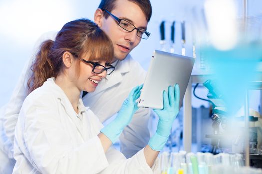 Attractive young female research scientist and her post doctoral male supervisor looking at the tablet in the life science (forensics, microbiology, biochemistry, genetics, oncology...)laboratory.