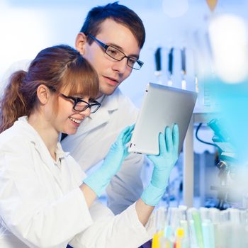 Attractive young female research scientist and her post doctoral male supervisor looking at the tablet in the life science (forensics, microbiology, biochemistry, genetics, oncology...)laboratory.