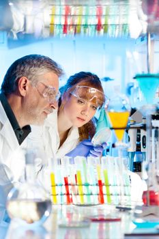 Attractive young female scientist and her senior male supervisor looking at the cell colony grown in the petri dish in the life science research laboratory (biochemistry, genetics, forensics, microbiology..)