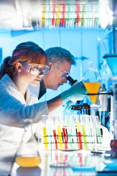 Attractive young female scientist and her senior male supervisor pipetting and microscoping in the life science research laboratory (biochemistry, genetics, forensics, microbiology..)