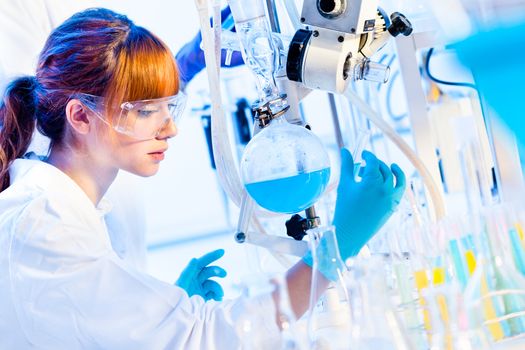 Chemical laboratory scene: attractive young PhD student scientist observing the blue indicator color shift after the solution  destillation.