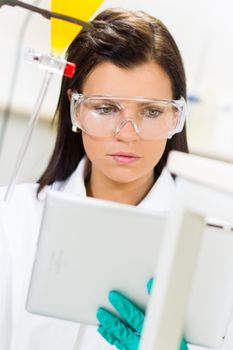Attractive young female scientist checking experiment protocol at tablet laptop computer in the life science research laboratory (bichemistry, genetics, forensics, microbiology..)