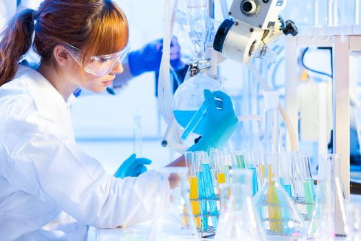 Chemical laboratory scene: attractive young PhD student and her post doctoral supervisor scientist observing the blue indicator color shift after the solution  destillation.