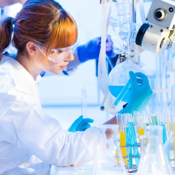 Chemical laboratory scene: attractive young PhD student and her post doctoral supervisor scientist observing the blue indicator color shift after the solution  destillation.