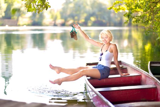 Carefree young blonde woman enjoying the sunny summer day on a vintage wooden boats on a lake in pure natural environment on the countryside.