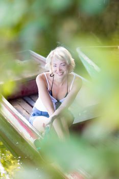 Relaxed young blonde woman  enjoying the sunny summer day on a vintage wooden boats on a lake in pure natural environment on the countryside.