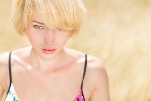 A portrait of a casual dressed beautiful young Caucasian woman outdoor in the meadow on a sunny summer day.