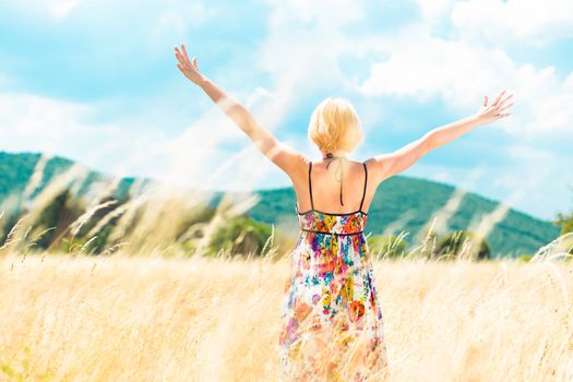 Lady enjoying the nature. Young woman arms raised enjoying the fresh air in summer meadow.