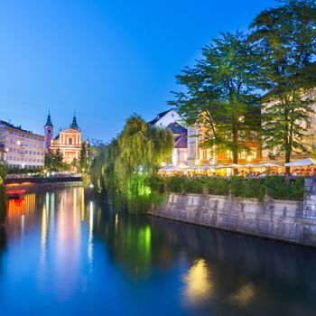 Romantic medieval Ljubljana's city center, the capital of Slovenia, Europe. Night life on the banks of river Ljubljanica, where many bars and restavrants take place. Franciscan Church of the Annunciation in the distance.