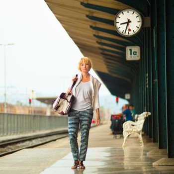 Blonde caucasian woman waiting at the railway station carrying bag.