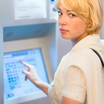 Lady buying a railway ticket at the automatic ticket vending machine with touch screen.