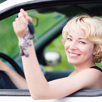 Woman, driving showing car keys out the window. Young female driving happy about her new car or drivers license. Caucasian model.