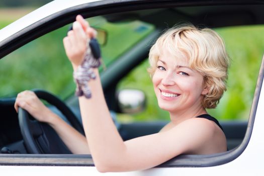 Woman, driving showing car keys out the window. Young female driving happy about her new car or drivers license. Caucasian model.