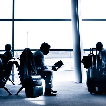 Silhouettes of businessman traveling on airport; waiting at the plane boarding gates.