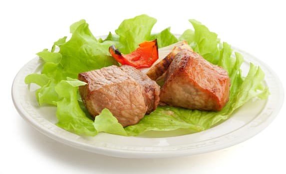 Two pieces of roasted meat with onion, paprika and fresh lettuce on the white plate
