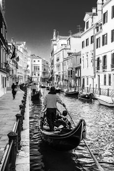 Gondolas passing on small canal among old historic houses and bridge in Venice, Italy. Black and white image.