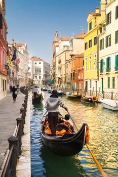 Vertical oriented image of gondolas passing on small canal among old historic houses and bridge in Venice, Italy.