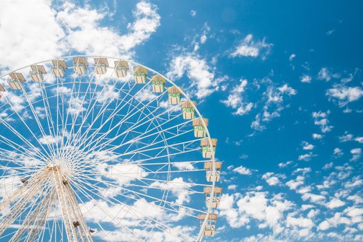 Ferris wheel of fair and amusement park.  White clouds in the blue sky in background.