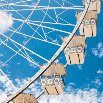 Ferris wheel of fair and amusement park.  White clouds in the blue sky in background.