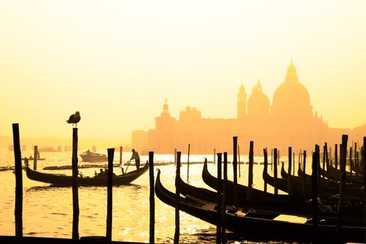 Romantic Italian city of Venice (Venezia), a World Heritage Site: traditional Venetian wooden boats, gondolier and Roman Catholic church Basilica di Santa Maria della Salute in the misty background.