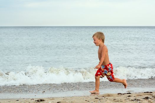 Little boy running at the shore near the sea
