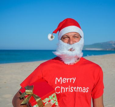 Portrait of young men in Santa hat with gift on tropical vacation
