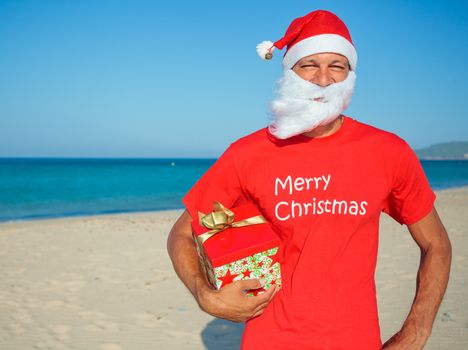 Young men in Santa hat with gift on tropical vacation