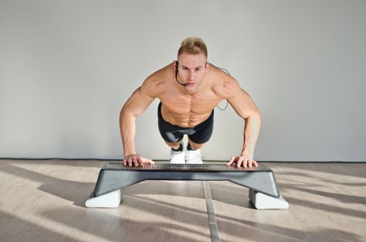 Young aerobics male coach shirtless leaning on step teaching class