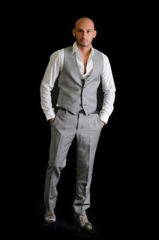 Elegant, bald young man in business suit on dark background, looking at camera