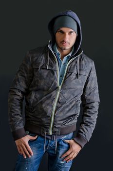 Trendy young man in winter clothes, jeans and hoodie, studio shot on dark background