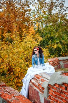 Beautiful bride in wedding dress and denim jacket in autumn park