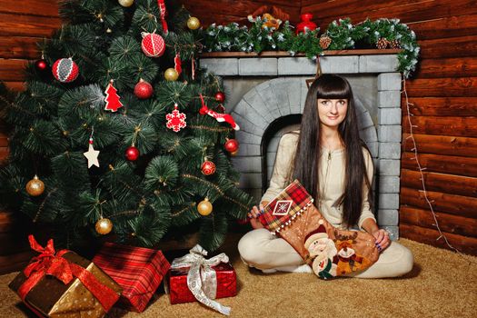 Attractive young woman holding gift and sits near Christmas tree