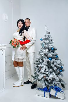 Young loving married couple near Christmas tree with gifts