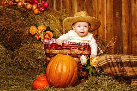 Little girl in straw hat sitting in a wicker basket near pumpkins