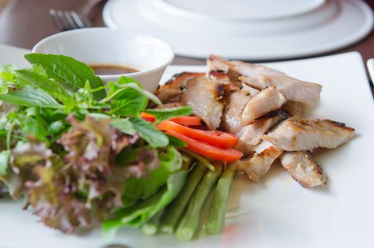 slice grilled pork  served with fresh vegetable on white dish