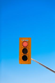 Single red traffic light demanding drivers to stop against blue sky with lots of copyspace
