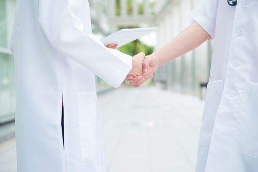 Two medical doctors shaking hands at hospital corridor, teamwork concept.