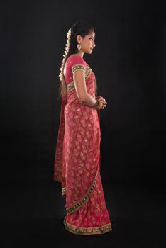 Full body side view or profile of traditional young Indian girl in sari costume standing isolated on black background.