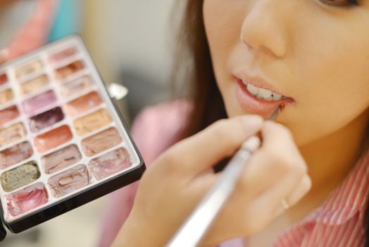 Young beautiful Asian bride applying wedding make-up by make-up artist. Focus on lips. 