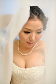 Beautiful Asian bride smiling under the veil on wedding day.