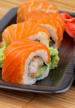 Arrangement of Philadelphia Rolls with Marinated Ginger and Wasabi on Black Plate closeup on Straw mat background